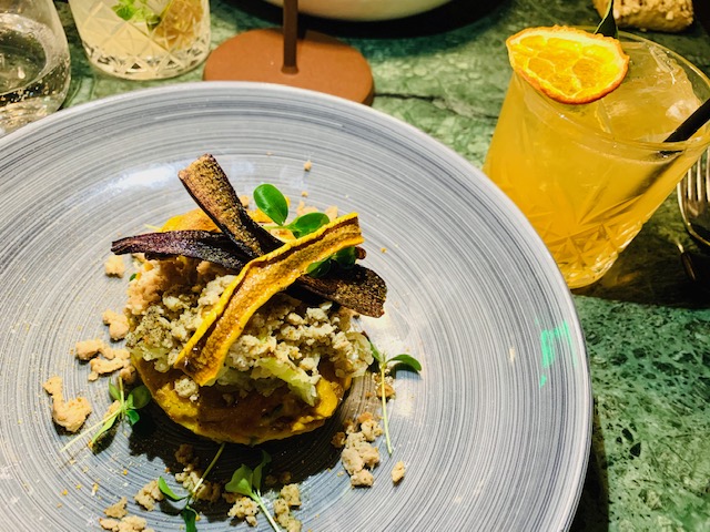 Lasagnetta alla besciamella di curcuma, zucchina croccante, luganega e porro, chips di carote accompagnato da un cocktail a base Gin con Aperol, sherbet di agrumi, shrub di albicocche